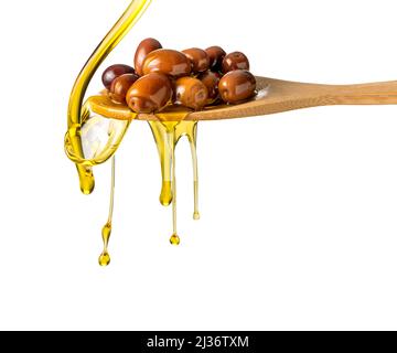 Natives Olivenöl extra tropft und spritzt aus einem Holzlöffel mit Oliven, isoliert auf einem weißen, schneidenen Pfad Stockfoto