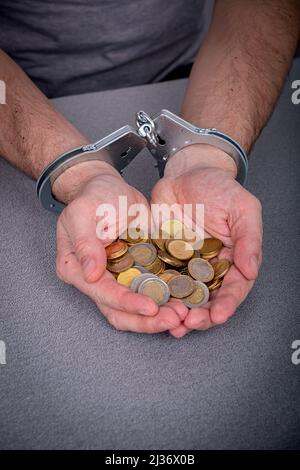 Männerhände in Handschellen mit einer Handvoll Münzen Stockfoto