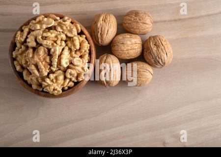 Geschälte Walnüsse und ganze Walnüsse auf Holzgrund Stockfoto