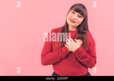 Ziemlich dunkelhaarige kaukasische Frau neigt ihren Kopf und hält ihre Hände auf Herz isoliert Studio Schuss Kopie Raum Medium Schuss . Hochwertige Fotos Stockfoto