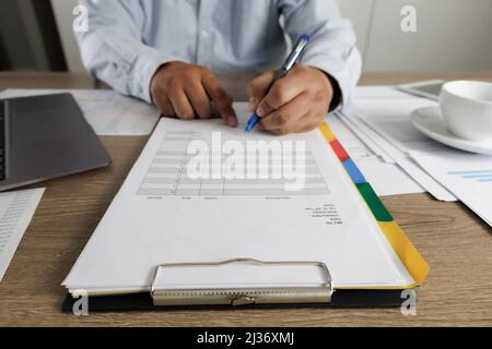 Geschäftsmann, der Dokumente liest, die den Vertrag auf Papier unterzeichnen, Geschäftsdokumente, die am Laptop auf dem Schreibtisch arbeiten, aus nächster Nähe Stockfoto