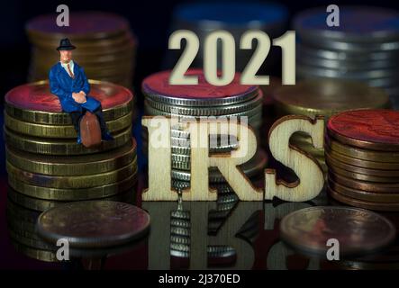 Miniaturmenschen. Mann, der auf Münzstapeln mit Text sitzt. IRS Taxman-Konzept. Stockfoto