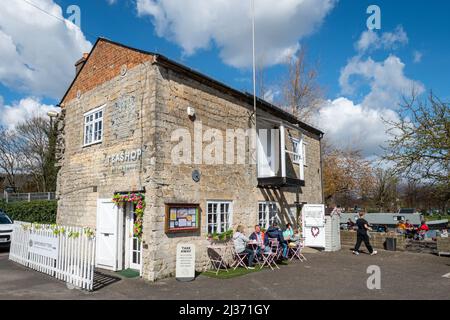 Menschen, die an Tischen vor dem Teeshop am Kanal, am Kennet- und Avon-Kanal im Stadtzentrum von Newbury, in der englischen Grafschaft Bekshire, sitzen Stockfoto