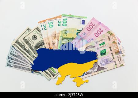 Die in Blau und Gelb gestrichene Landkarte der Ukraine liegt auf Geldscheinen, Dollars, Euros und Griwna auf weißem Grund. Hilfe von westlichen Partnern im Stockfoto