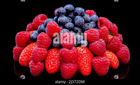 Erdbeeren, Himbeeren und Heidelbeeren auf schwarzem Hintergrund. Frische, lebendige Bio-Sommerbeeren, Nahaufnahme. Roher veganer Sommerjause. Stockfoto