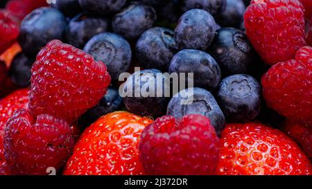 Erdbeeren, Himbeeren und Heidelbeeren auf schwarzem Hintergrund. Frische, lebendige Bio-Sommerbeeren, Nahaufnahme. Roher veganer Sommerjause. Stockfoto