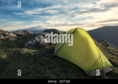 Grünes Zelt auf dem felsigen Gipfel des Nebrodi Parks, auf dem Hintergrund schneebedeckter Ätna-Berg und Wolkenlandschaft, Sizilien Stockfoto