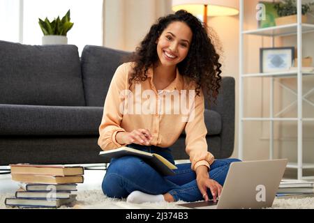 Harte Arbeit leisten. Aufnahme einer jungen Frau, die sich Notizen macht, während sie von zu Hause aus auf ihrem Laptop arbeitet. Stockfoto