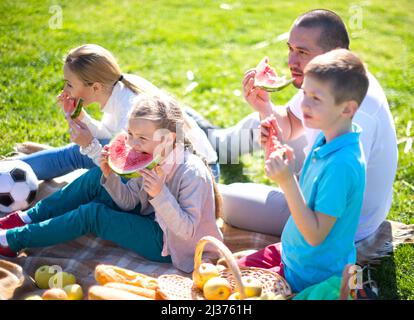 Glückliche Eltern mit Kindern auf Picknick essen Wassermelone im Sommerpark Stockfoto