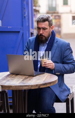 Ein erwachsener Mann, der mit seinem Laptop im Café draußen Kaffee getrunken hat Stockfoto