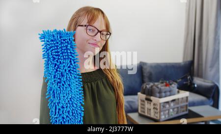 Kaukasische Hausfrau mittleren Alters mit langen, rothaarigen Haaren, die die Kamera anschaut und blauen Mopp in der Nähe ihres Gesichts hält. Hochwertige Fotos Stockfoto