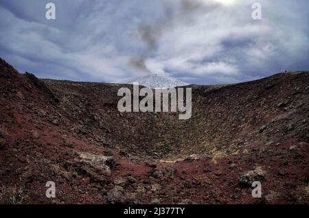 Rotes vulkanisches Gestein aus altem Krater und dunkler Rauch vom Ätna-Berg in dramatischem Himmel, Sizilien Stockfoto