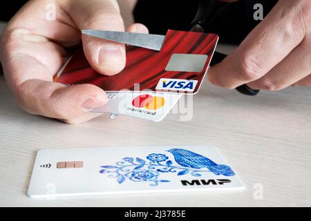 2. April 2022. Barnaul. Russland: Ein Mann schneidet Bankkarten dieser Art und mastercard mit einer Schere. Zerstörung von Plastikkarten nach den expirati Stockfoto