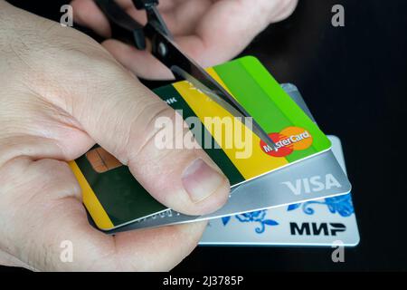 2. April 2022. Barnaul. Russland: Ein Mann schneidet Bankkarten dieser Art und mastercard mit einer Schere. Zerstörung von Plastikkarten nach den expirati Stockfoto