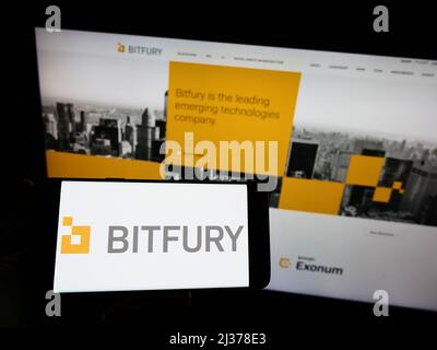 Person, die das Smartphone mit dem Logo des niederländischen Blockchain-Unternehmens Bitfury Holding B.V. auf dem Bildschirm vor der Website hält. Konzentrieren Sie sich auf die Telefonanzeige. Stockfoto