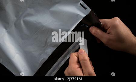 Abreißen von klebrigen Versandtaschen, männliche Hände, die das Produkt für den Versand vorbereiten, isoliert auf schwarzem Hintergrund, Draufsicht Stockfoto