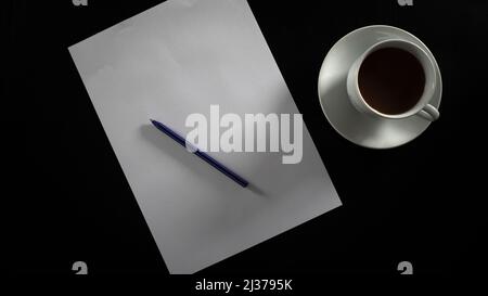 Filterkaffee zum Schreiben und Trinken in weißer Tasse und Untersetzer, leeres Papier und Stift, isoliert auf schwarzem Hintergrund, Draufsicht Stockfoto