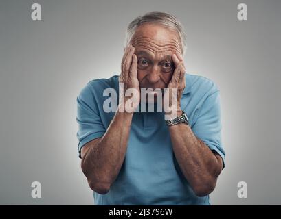 Der Stress könnte mich einfach umbringen. Aufnahme eines älteren Mannes, der in einem Studio vor grauem Hintergrund die Hände an sein Gesicht klammert. Stockfoto