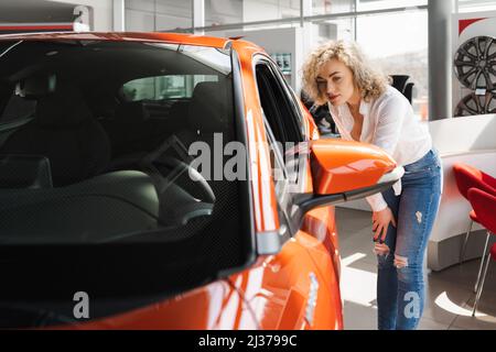 Lockiges Blondine in einem Autohaus. Frau wählt ein neues Auto Stockfoto