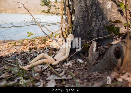 Holzfiguren sitzen vor dem Baumkörper, Holzpuppe machen ein Nickerchen im Wald, Seitenansicht, entspannend und kühlend, Herbstkonzept Stockfoto