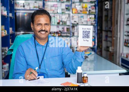 Glücklicher Apotheker zeigt Scan hier QR-Code-Schild für den Kauf bezahlen, indem er Kamera im Einzelhandel medizinischen Speicher- Konzept der bargeldlosen Zahlung suchen Stockfoto