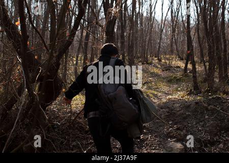 Mann, der auf einem schlammigen und holprigen Weg durch Wald, schlammige und felsige Straße in der Natur geht, ein junger Mann mit einem Rucksack, der umherstreift Stockfoto