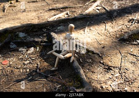 Hölzerne Schaufensterpuppe sitzen auf Baumwurzeln Blick auf den Wald, Holzpuppe Beine gekreuzt, Seitenansicht, Herbst-Konzept, Wald Hintergrund Stockfoto