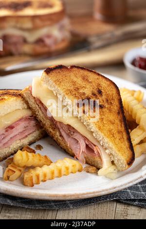 Gegrilltes Schinken- und Käsesandwich in zwei Hälften geschnitten mit pommes auf einem Teller Stockfoto