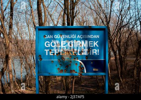 Blaues Warnschild mit Einschusslöchern, ein Schild mit einem Loch in der Natur, ein zerstörtes Warnschild in einem Wald Stockfoto