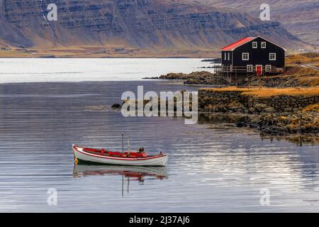 Kleines Boot und schwarzes Holzhaus, Djupivogur, Eastfjords, Island. Landschaft im Herbst mit Berghintergrund aufgenommen. Stockfoto