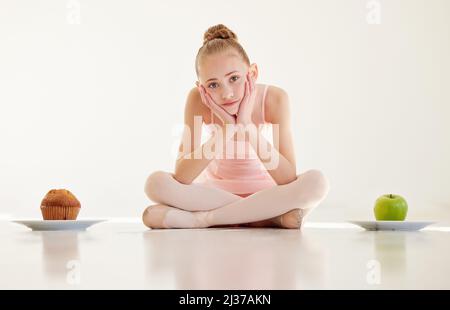 Sie verletzen, indem Sie sich verhungern. Aufnahme einer jungen Ballerina, die entscheidet, was sie in einem Studio essen soll. Stockfoto