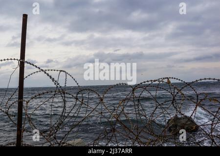 Verrostete Stacheldrähte vor dem bewölkten Meer, welliges Meer mit Stacheldraht, Freiheitsidee, Sturmwetter, Vorderansicht Stockfoto