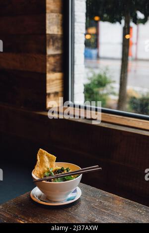 Thai Victory Nudeln in Schüssel mit Essstäbchen auf Restauranttisch am Fenster während des Tages Stockfoto