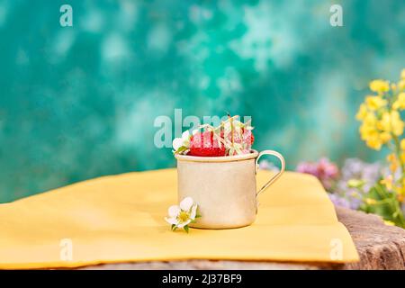 Erdbeeren in einem Metall-Aluminium-Reisebecher auf Stumpf. Grüner und gelber Sommerhintergrund. Cottagecore Ästhetik Konzept, trendige Schatten Hintergrund. C Stockfoto