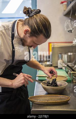 Eine vertikale Aufnahme eines Mannes, der in einer Küche mit Tintenfisch und rotem Paprika kocht Stockfoto