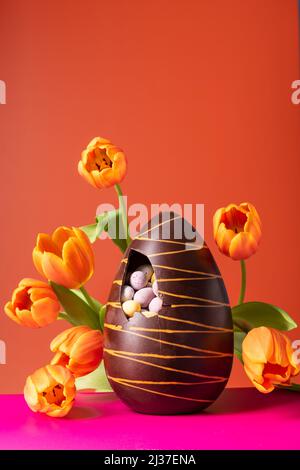 Osterschokoladenei mit Frühlingszwiespelzen auf leuchtendem orangefarbenem Hintergrund Stockfoto