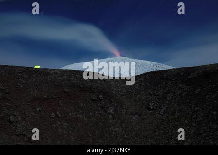 Beleuchtete Zelt am Rande eines alten Krater vor dem schneebedeckten Ätna, die vulkanischen Dampf emittieren, Ätna Park - Sizilien Stockfoto