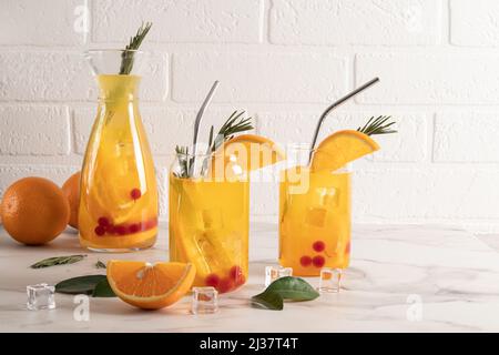 Obst kohlensäurehaltiges Vitaminwasser in zwei modernen Gläsern in Form einer Dose, in einer Karaffe auf einem Marmortisch gegen eine weiße Ziegelwand. Entgiftung