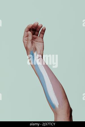 Der Arm eines jungen Menschen mit der Transgender-Pride-Flagge, die darin gemalt ist, auf einem hellgrünen Hintergrund Stockfoto