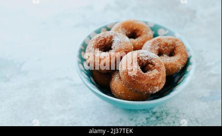 Nahaufnahme einiger hausgemachter Rosquillas, typisch spanischer Donuts mit Zucker bestreut, in einer blauen Keramikschale, auf einer Steinoberfläche Stockfoto