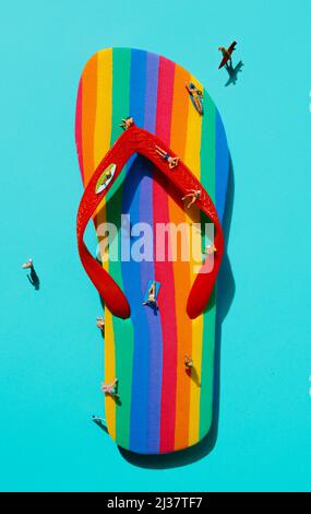 Ansicht einiger Miniatur-Männer, die Badeanzug tragen, auf einem Flip-Flop mit Regenbogenmuster und blauem Hintergrund Stockfoto