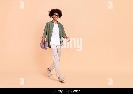 In voller Länge Körpergröße Ansicht der attraktiven fröhlich qualifizierten Kerl gehen halten Laptop Startup-Projekt isoliert über beige Pastellfarben Hintergrund Stockfoto