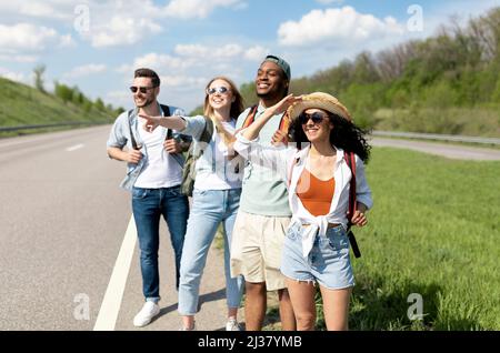 Eine Gruppe von glücklichen Freunden, die am Straßenrand stehen, im Sommerurlaub mitfahren, auf dem Land unterwegs sind und das Auto anhalten Stockfoto