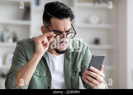 Konzept Der Sehprobleme. Junger Arabischer Mann In Einer Brille Beim Betrachen Des Smartphone-Bildschirms Stockfoto