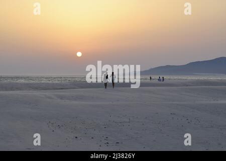 Touristen, die am Strand Playa de Los Lances bei Sonnenuntergang in Tarifa Andalusien Spanien spazieren gehen. Stockfoto