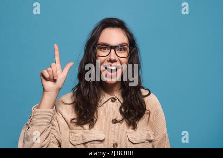 Glücklich aufgeregt tausendjährige europäische Frau in einer Brille mit offenem Mund zeigt Daumen auf freiem Raum Stockfoto