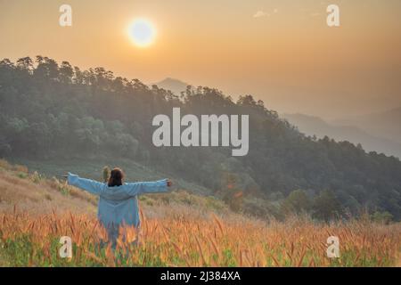 Rückansicht einer glücklichen Frau im goldenen Wiesenfeld bei Sonnenaufgang. Stockfoto