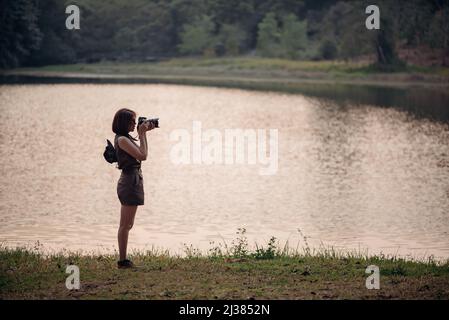 Eine Abenteurerin fotografiert den See und den Pinienwald. Stockfoto