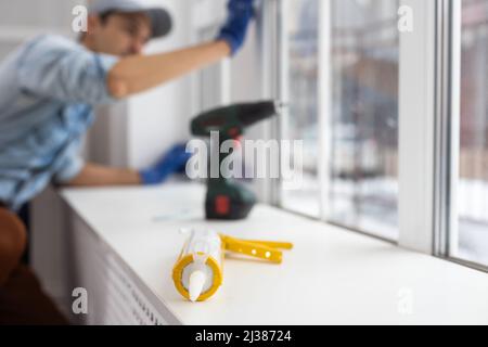 Silikon-Klebepistole, Bauarbeiter Installation Fenster im Haus. Handwerker, der das Fenster mit einem Schraubendreher fixiert Stockfoto