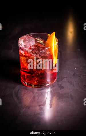 Eine vertikale Aufnahme eines Negroni-Cocktails in einem Retro-Glas mit Eis und Orangenschale auf dunklem Hintergrund Stockfoto